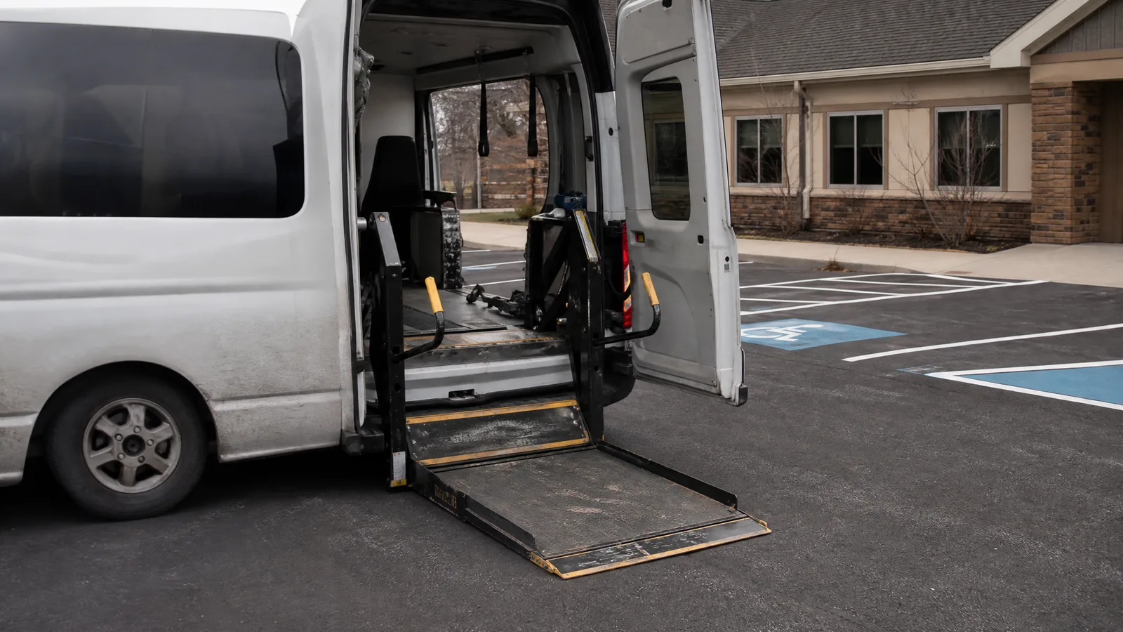 Side-entry van with its wheelchair lift platform deployed and lowered to the pavement, restraint straps visible inside